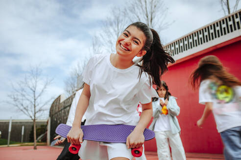 Fröhliches Teenager-Mädchen mit Skateboard auf dem Spielplatz - MDOF01176