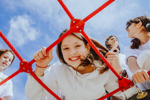 Glückliches Mädchen im Teenageralter mit Freunden, die auf dem Klettergerüst auf dem Spielplatz spielen - MDOF01202