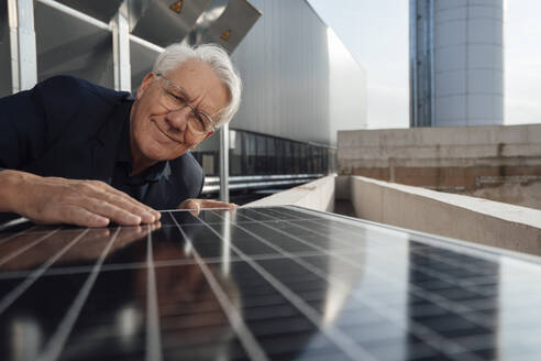 Lächelnder älterer Geschäftsmann bei der Prüfung eines Solarpanels - JOSEF19340