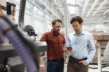 Businessmen discussing over smart phone in factory - JOSEF19358