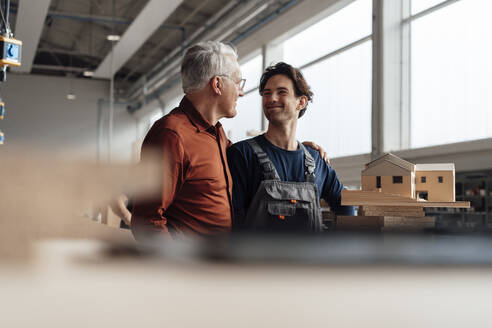 Smiling businessmen together standing with house model in industry - JOSEF19383