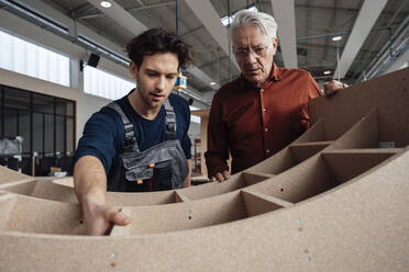 Carpenter with colleague examining furniture in industry - JOSEF19391