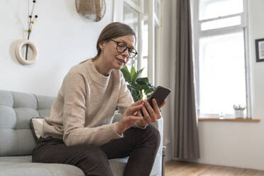 Ältere Frau benutzt Smartphone auf dem Sofa zu Hause - VPIF08081