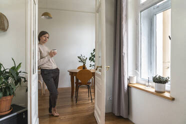 Thoughtful mature woman with coffee cup standing by door - VPIF08084