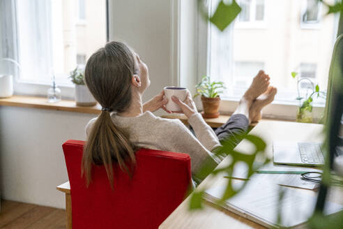 Mature freelancer with coffee cup sitting at desk - VPIF08100