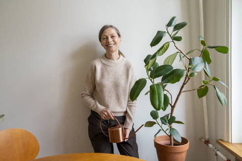 Happy woman leaning on wall with watering can - VPIF08105