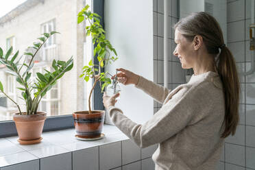 Happy mature woman spraying water on plants in bathroom - VPIF08107