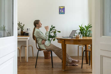 Nachdenklicher reifer Freiberufler sitzt mit Kaffeetasse zu Hause - VPIF08132
