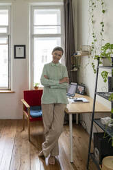 Happy freelancer standing by desk at home - VPIF08140