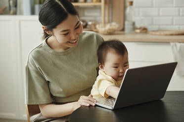 Happy freelancer mother with daughter using laptop at home - KPEF00005