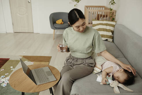 Freelancer mother stroking daughter sleeping on sofa at home - KPEF00025