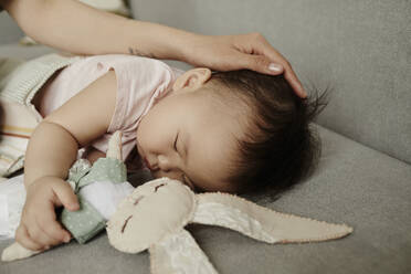 Mother stroking daughter sleeping with stuffed toy on sofa at home - KPEF00026