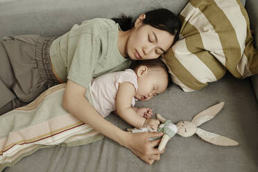 Mother and daughter sleeping together on sofa at home - KPEF00031