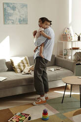 Father lulling daughter standing in living room at home - KPEF00036