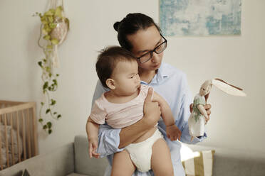 Father showing stuffed toy to daughter at home - KPEF00038