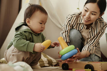 Mother giving toy to daughter crouching at home - KPEF00043