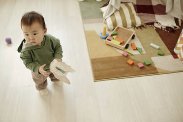 Daughter holding stuffed toy standing on floor at home - KPEF00045