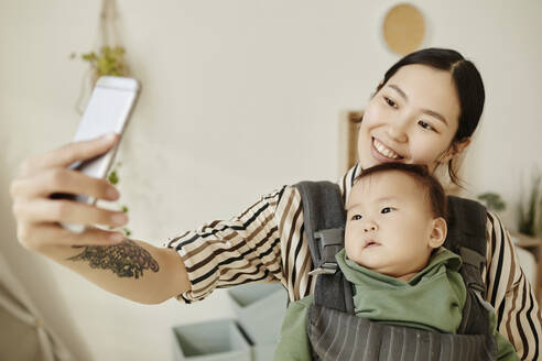 Eine fröhliche Mutter fängt einen kostbaren Moment mit ihrer Tochter ein, indem sie ein Smartphone für ein Selfie zu Hause benutzt - KPEF00053