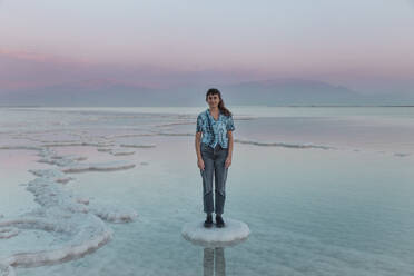 Lächelnde junge Frau, die auf einer Salzformation im Toten Meer steht - PCLF00627