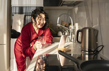 Glückliche reife Frau mit einem Glas Wasser im Gespräch über Videoanruf durch Smartphone - ADF00090