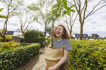 Cheerful girl standing with avocado plant on footpath - IHF01363