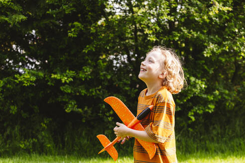 Lächelnder blonder Junge mit Flugzeugspielzeug im Park - IHF01379