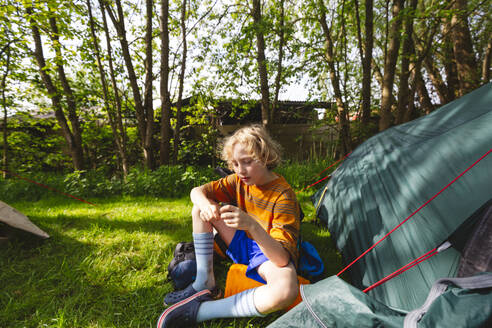 Junge sitzt bei einem Zelt im Park - IHF01380