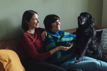 Smiling lesbian couple playing with dog at home - JOSEF19454