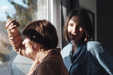 Lesbian couple standing near window at home - JOSEF19455