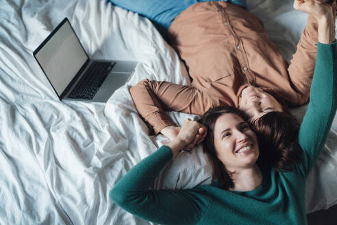 Glückliches lesbisches Paar auf dem Bett liegend mit Laptop zu Hause - JOSEF19456