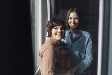 Happy lesbian couple standing near window at home - JOSEF19460