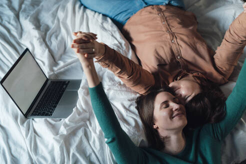 Happy lesbian couple lying down on bed at home - JOSEF19499