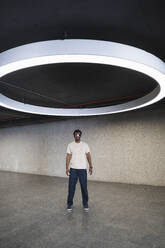 Young man with futuristic cyber glasses standing under modern ring lamp - PNAF05284