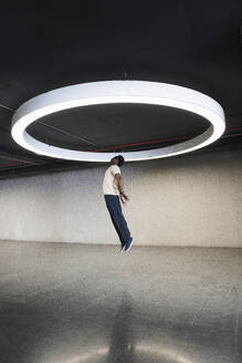 Young man with futuristic cyber glasses jumping under modern ring lamp - PNAF05286
