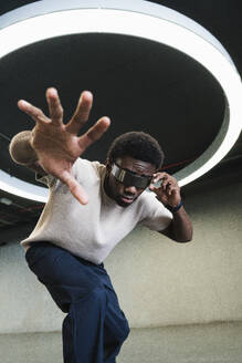 Young man with futuristic looking through cyber glasses under modern ring lamp reaching out hand - PNAF05292