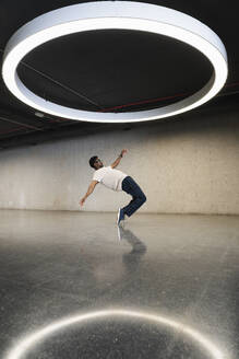 Young man with futuristic cyber glasses break dancing under modern ring lamp - PNAF05294