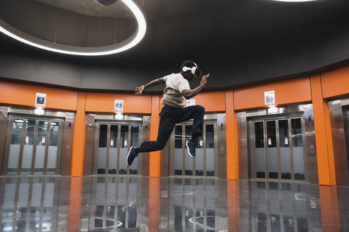 Young man wearing Virtual Reality Simulator jumping at Metro Station - PNAF05305