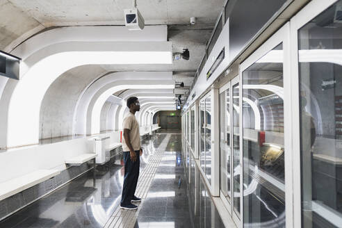 Man wearing futuristic glasses standing at metro station - PNAF05306