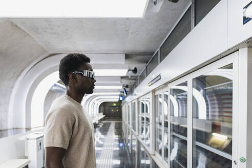 Man wearing futuristic glasses standing at metro station - PNAF05307