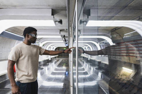 Young man with cyber glasses touching glass pane with his forefinger - PNAF05308