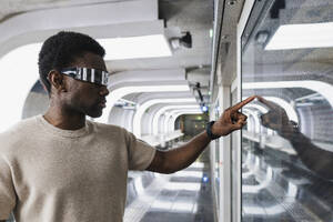 Young man with cyber glasses touching glass pane with his forefinger - PNAF05313