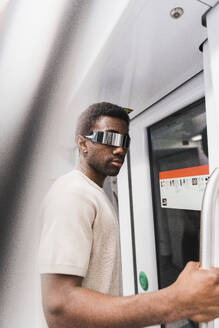 Young man wearing cyber glasses standing in metro train - PNAF05316