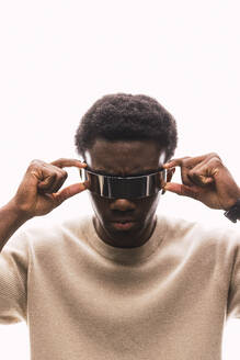 Cool young man adjusting cyber glasses against white background - PNAF05339