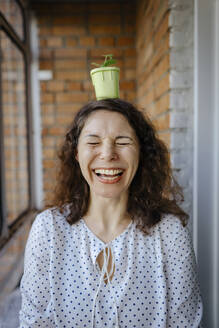 Cheerful woman standing with potted plant on head - IEF00436