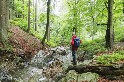 Reife Frau mit Rucksack im Wald stehend - GWF07819