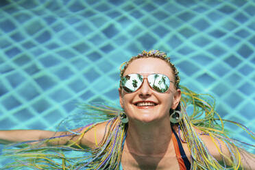 Glückliche Frau mit Sonnenbrille entspannt im Schwimmbad - IEF00437