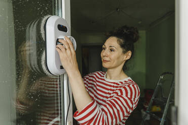 Frau reinigt Fenster mit Waschroboter - IEF00450