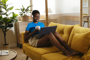 Happy young freelancer with coffee cup working on laptop at home - EBSF03426