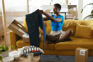 Woman checking denim jeans and unboxing packages at home - EBSF03431
