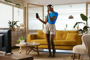 Happy young woman singing and listening to music at home - EBSF03434